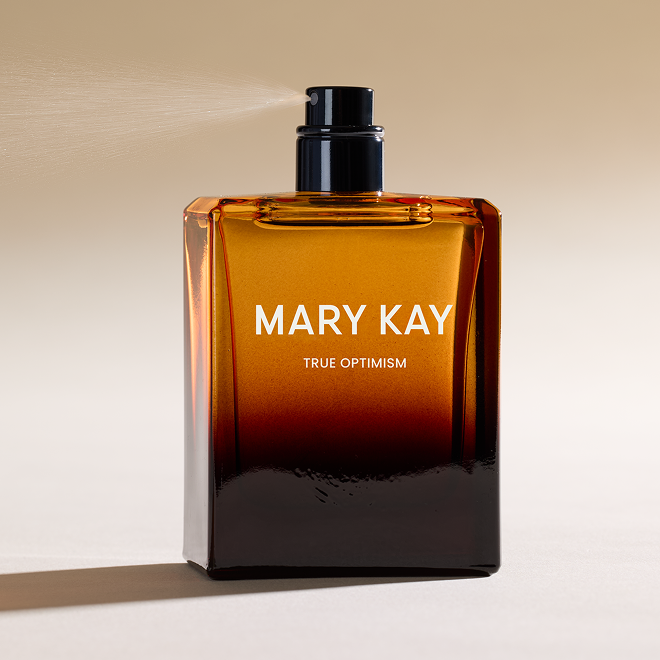 Bottle of Mary Kay True Optimism Eau de Parfum spritzing against tan background 